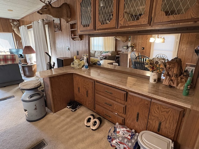 kitchen with glass insert cabinets, light colored carpet, wood walls, light countertops, and brown cabinets