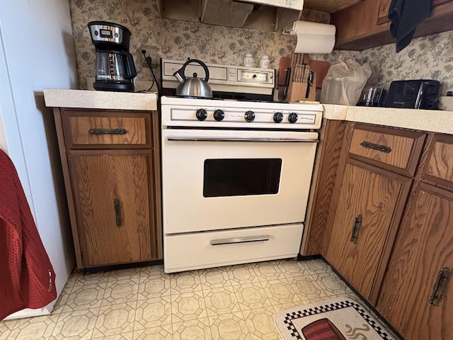 kitchen featuring light floors, electric range, light countertops, extractor fan, and brown cabinets