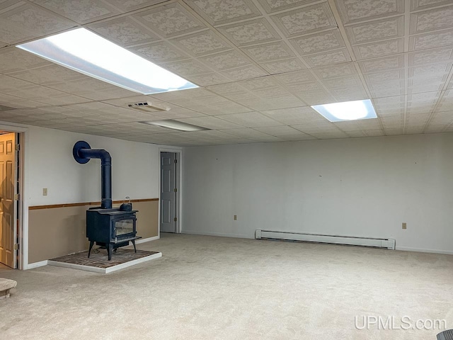 finished basement featuring a baseboard radiator, visible vents, a wood stove, and carpet flooring