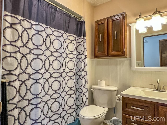 full bathroom with curtained shower, vanity, toilet, and wainscoting