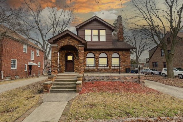 view of front of home with brick siding, a porch, and a chimney