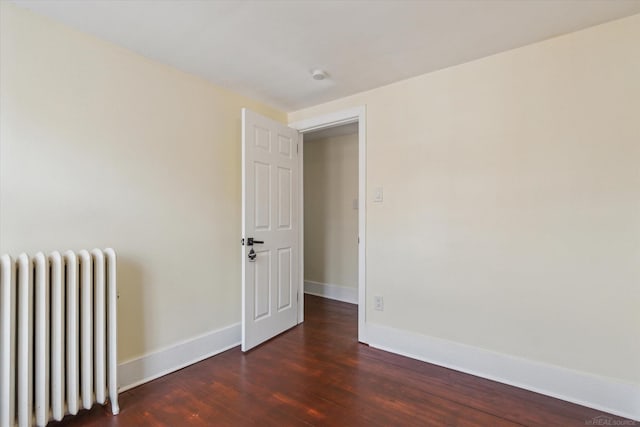 empty room featuring dark wood finished floors, radiator, and baseboards