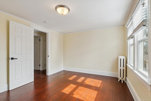 empty room featuring dark wood-style floors, radiator heating unit, and baseboards