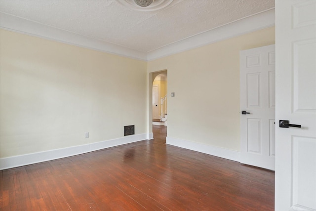 empty room featuring visible vents, a textured ceiling, dark wood-style floors, arched walkways, and baseboards