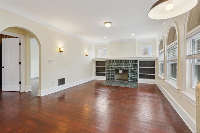 unfurnished living room featuring visible vents, baseboards, a tiled fireplace, hardwood / wood-style floors, and arched walkways