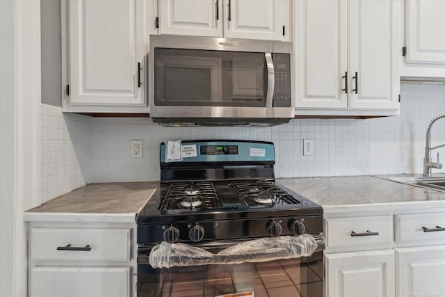 kitchen featuring stainless steel microwave, white cabinets, gas stove, and decorative backsplash