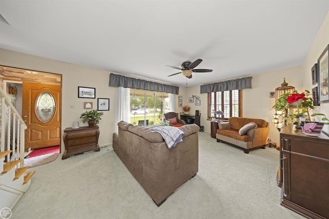 living room featuring stairway, light colored carpet, and ceiling fan