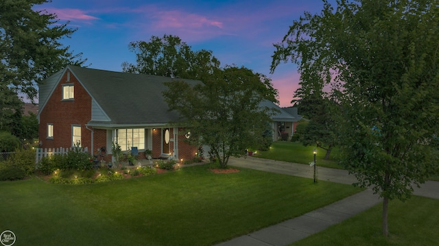 new england style home with a yard, brick siding, and driveway