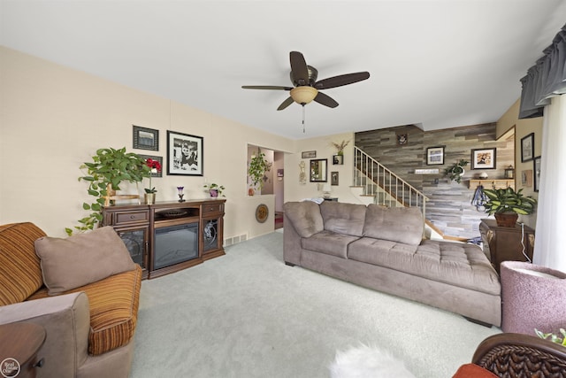 living area with visible vents, a ceiling fan, carpet flooring, a fireplace, and stairs