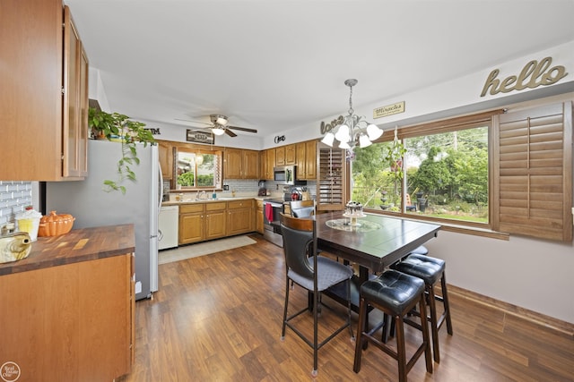 dining space featuring ceiling fan with notable chandelier and dark wood-style flooring