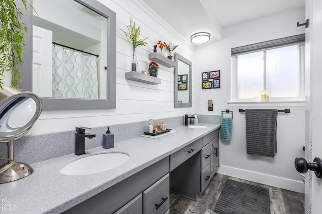 full bath featuring double vanity, wood finished floors, baseboards, and a sink