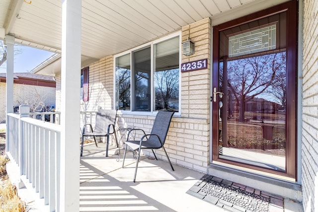 doorway to property with a porch and brick siding