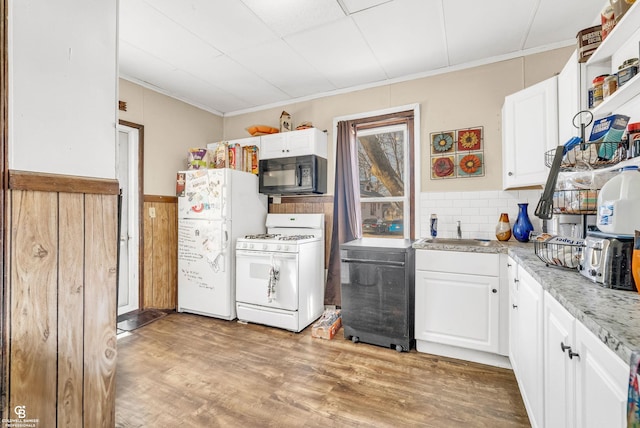 kitchen with light wood-type flooring, a wainscoted wall, a sink, white appliances, and white cabinets