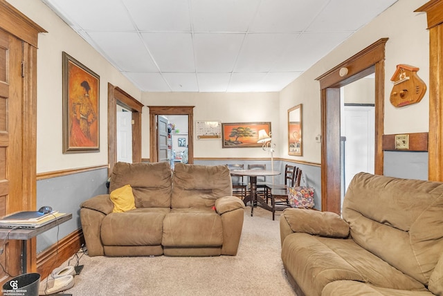 carpeted living room with a wainscoted wall and a drop ceiling