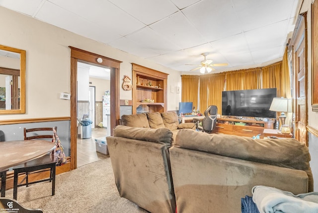 living area featuring built in shelves, light colored carpet, and ceiling fan