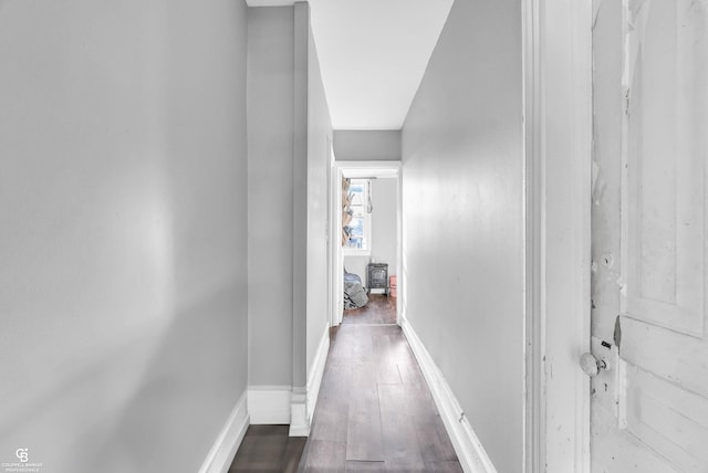 corridor featuring dark wood-type flooring and baseboards