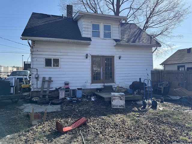 back of property with a chimney, roof with shingles, and fence