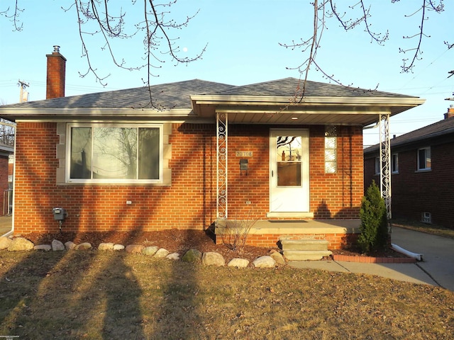 bungalow featuring brick siding, a chimney, and a shingled roof