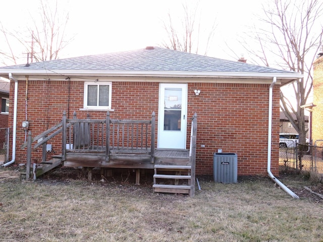 rear view of house with brick siding, a shingled roof, fence, a wooden deck, and central AC