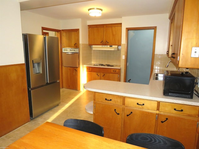 kitchen with a peninsula, oven, light countertops, stainless steel refrigerator with ice dispenser, and under cabinet range hood