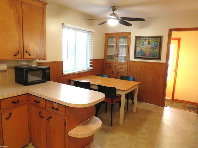 kitchen featuring a ceiling fan, a wainscoted wall, light countertops, black microwave, and wood walls