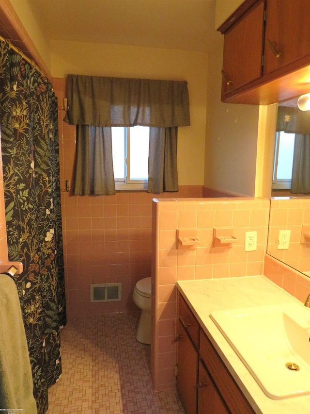 bathroom featuring visible vents, vanity, toilet, and tile walls