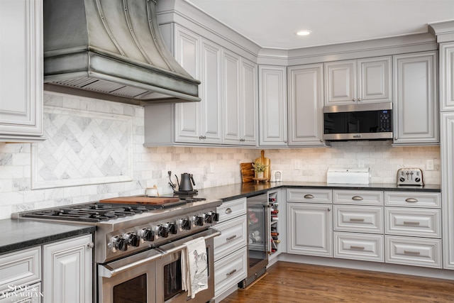 kitchen featuring stainless steel appliances, custom exhaust hood, dark countertops, and beverage cooler