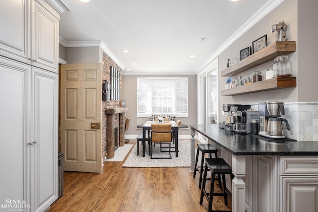 kitchen with open shelves, ornamental molding, light wood-style floors, a kitchen bar, and dark countertops