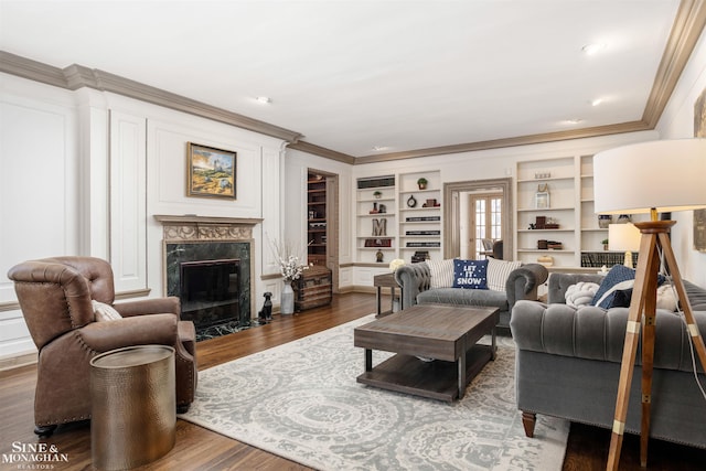 living room featuring built in features, a fireplace, wood finished floors, and ornamental molding