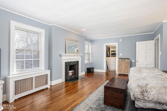 bedroom with radiator, wood finished floors, baseboards, a fireplace, and ornamental molding