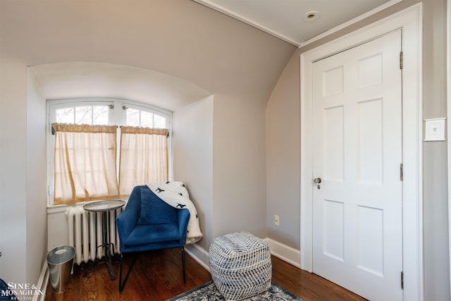 sitting room with radiator, wood finished floors, arched walkways, and baseboards