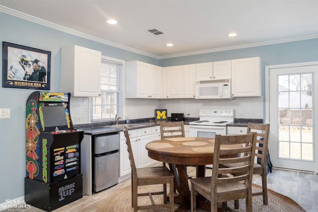 kitchen featuring white appliances, dark countertops, visible vents, white cabinetry, and crown molding