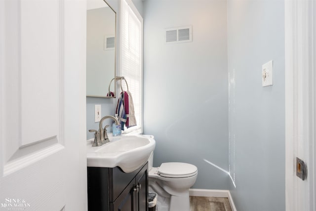 half bathroom featuring vanity, toilet, wood finished floors, and visible vents