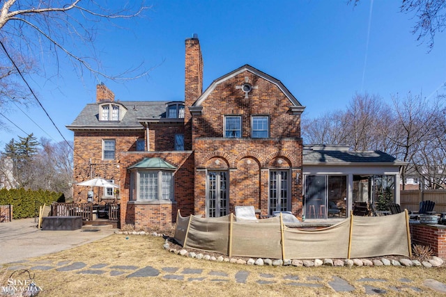 view of front of house with brick siding, a high end roof, a chimney, and fence