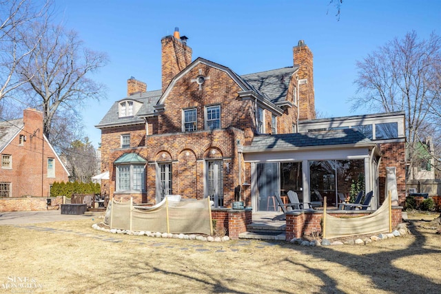 back of property featuring a high end roof, a yard, a chimney, a patio area, and brick siding