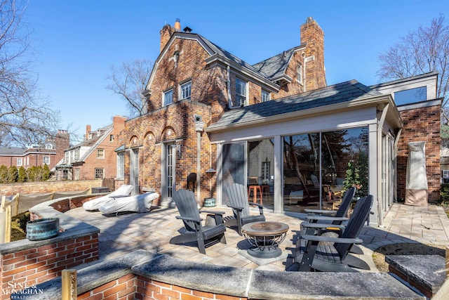 rear view of property featuring a patio, a high end roof, a chimney, a fire pit, and brick siding