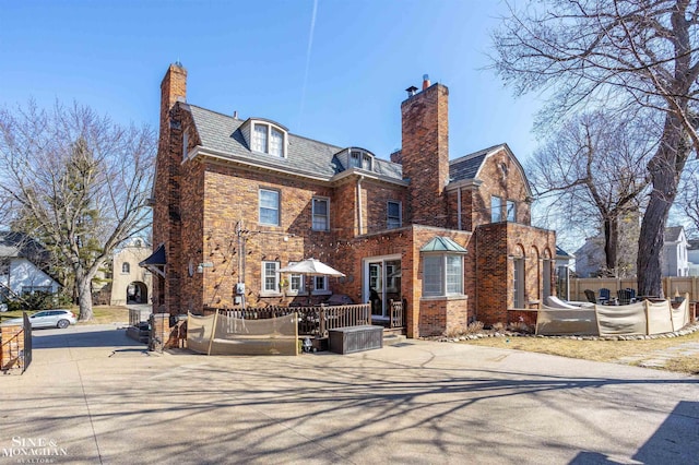 exterior space featuring a high end roof, brick siding, a chimney, and fence