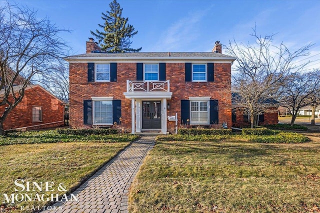 colonial house with brick siding, a front lawn, a balcony, and a chimney