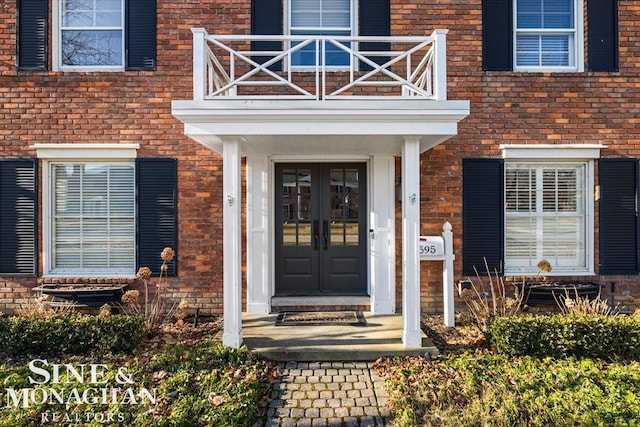 entrance to property with brick siding, french doors, and a balcony