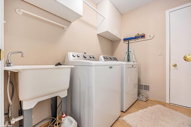 clothes washing area with visible vents, cabinet space, independent washer and dryer, and light wood finished floors