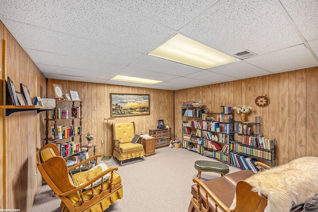 sitting room with wooden walls, a drop ceiling, visible vents, and carpet floors