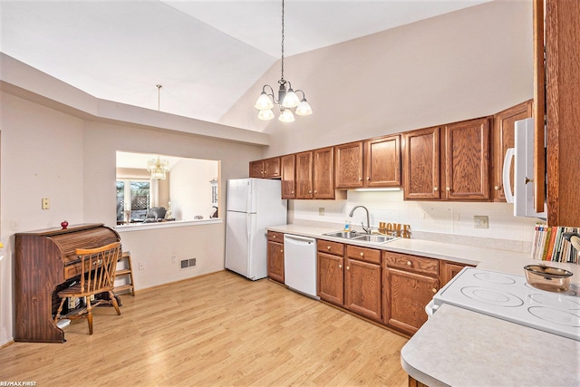 kitchen with a sink, white appliances, an inviting chandelier, and brown cabinetry