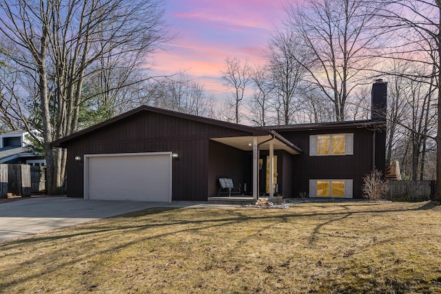 view of front of house with fence, driveway, a yard, a chimney, and a garage