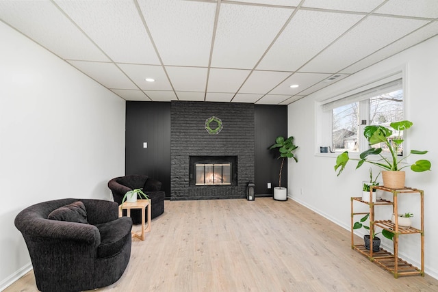 living area featuring light wood-type flooring, recessed lighting, baseboards, a fireplace, and a paneled ceiling