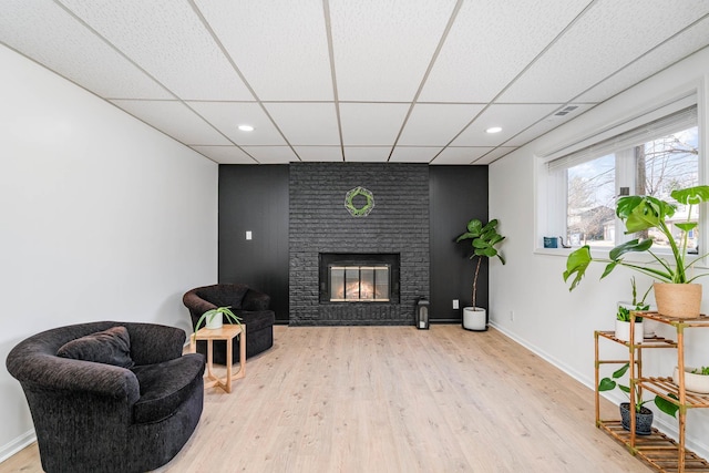 sitting room featuring wood finished floors, recessed lighting, baseboards, a paneled ceiling, and a brick fireplace