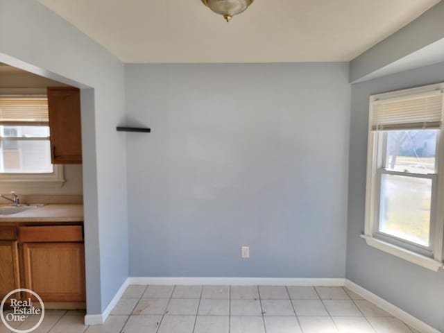 unfurnished dining area featuring light tile patterned floors, baseboards, and a sink