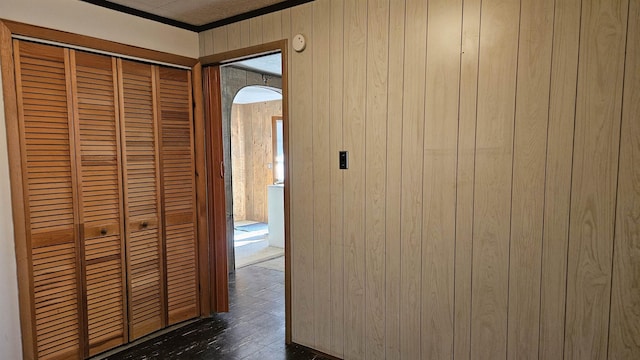 hallway with dark wood-style floors, arched walkways, wood walls, and crown molding