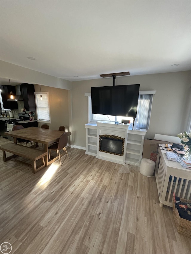 living area with light wood-type flooring, baseboards, and a glass covered fireplace