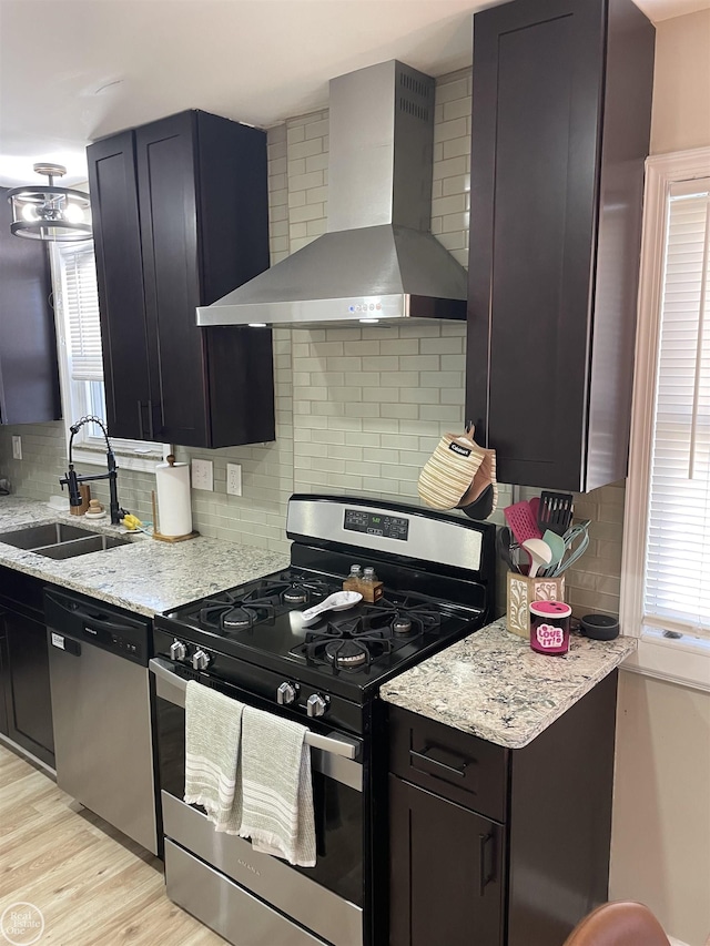 kitchen featuring wall chimney range hood, decorative backsplash, light wood-style floors, stainless steel appliances, and a sink