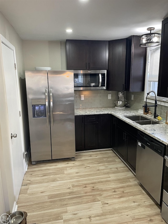 kitchen featuring a sink, dark cabinetry, stainless steel appliances, light wood-style floors, and light stone countertops